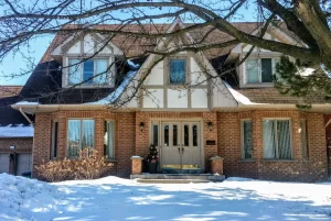 Brick residential home with snow-covered lawn and bare tree branches in front