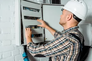 Electrician in a safety helmet inspecting a switchboard panel with electrical wiring