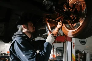 Mechanic using a work light while inspecting the wheel area under a lifted vehicle